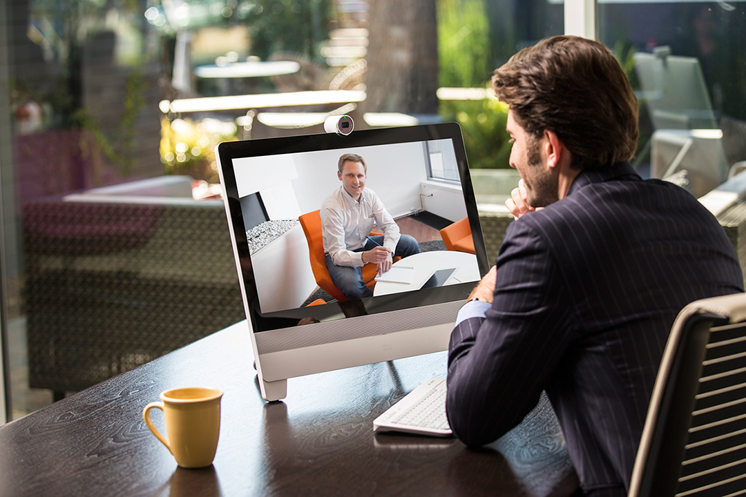 Individual using an IP phone connected to his desktop computer to participate in office communications.