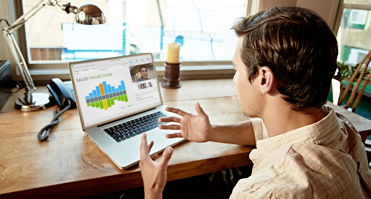 Young man using WebEx web conferencing via his laptop to connect with the office while working from home. BYOD (bring your own device) is a business trend more and more employees are leaning towards.